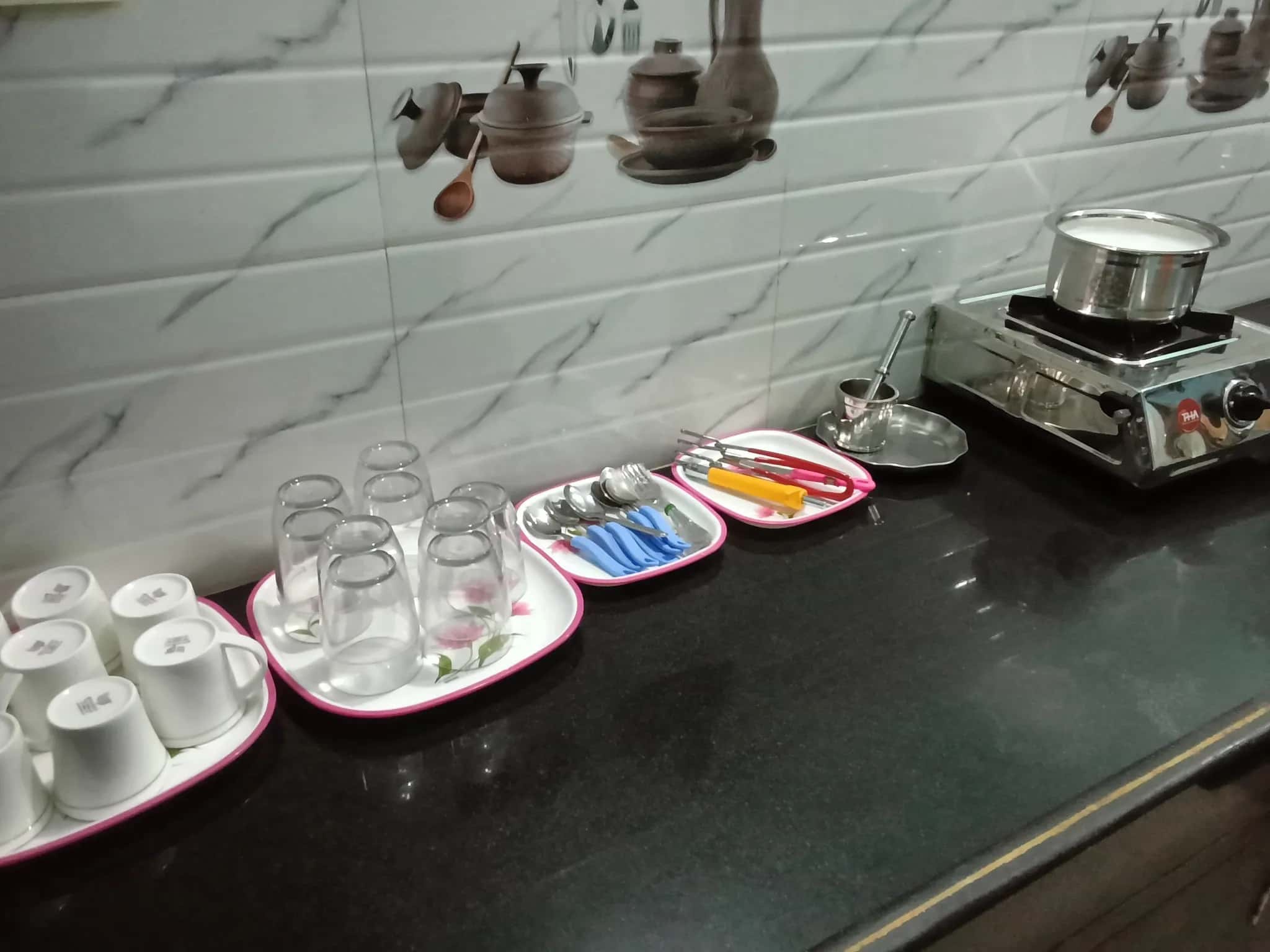 Kitchenette with granite countertop, tiled backsplash, ceramic mugs, glass tumblers, cutlery, and an induction cooktop.